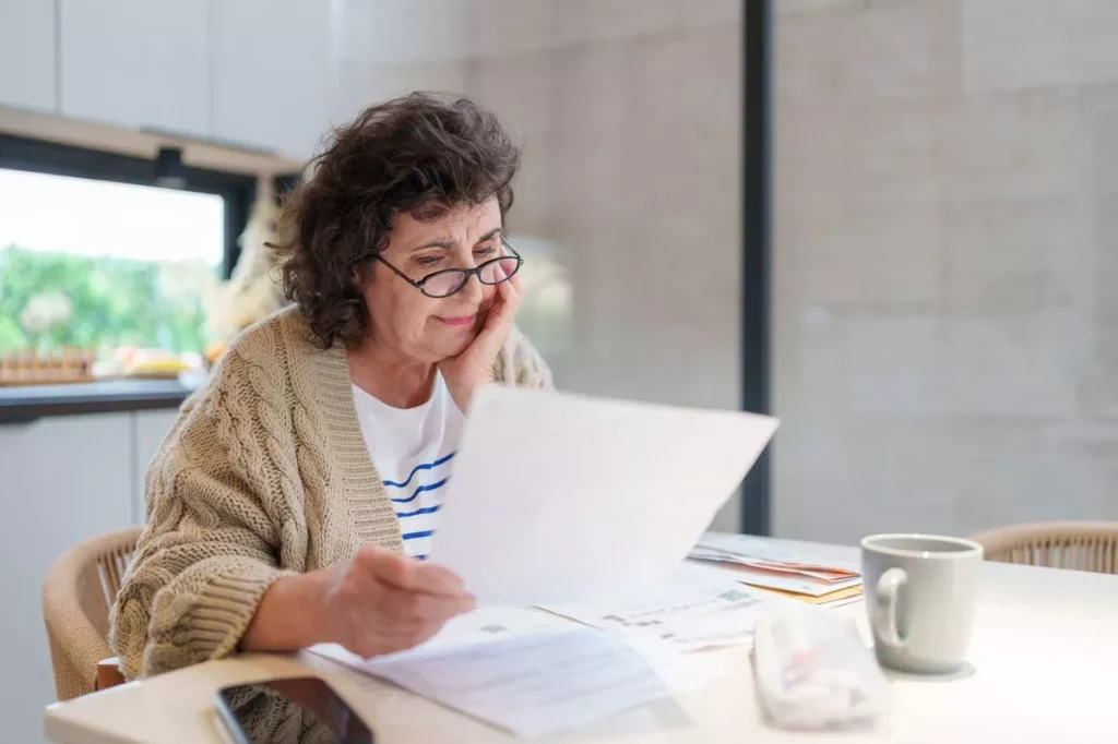 Stressed and Worried Senior Woman Calculating Domestic Expenses, Sitting at Dining Table in the kitchen, People, Accounting, Finances, Family Budget and Financial Issues Concept.